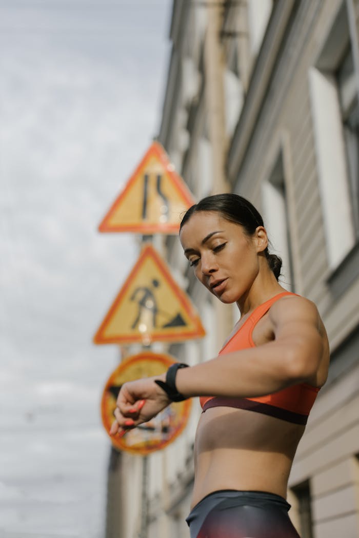 Fit woman in activewear checks her watch on an urban street, embodying fitness and lifestyle.